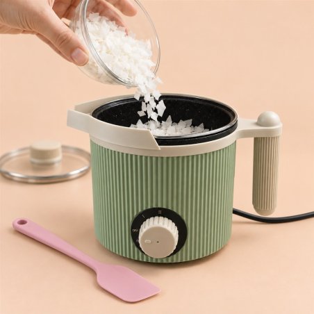 Mano añadiendo escamas blancas a un fundidor eléctrico verde abierto junto a una espátula