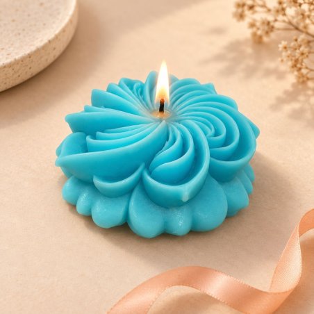 Vela turquesa acesa em forma de flor de dália junto a uma fita sobre fundo bege
