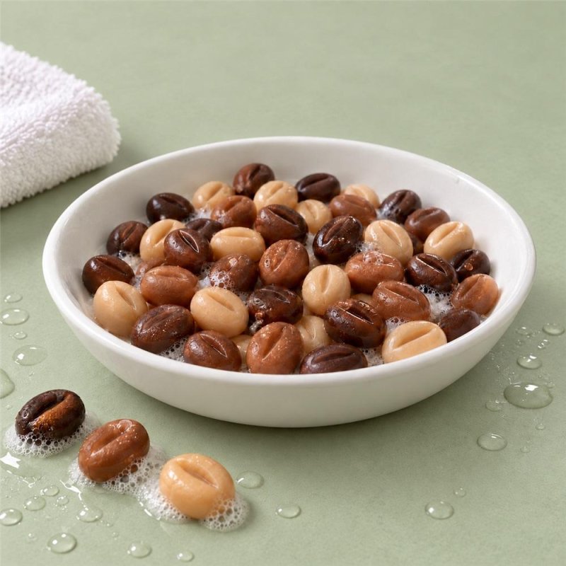 Petits savons en forme de grains de café bruns et crème avec de la mousse dans un bol