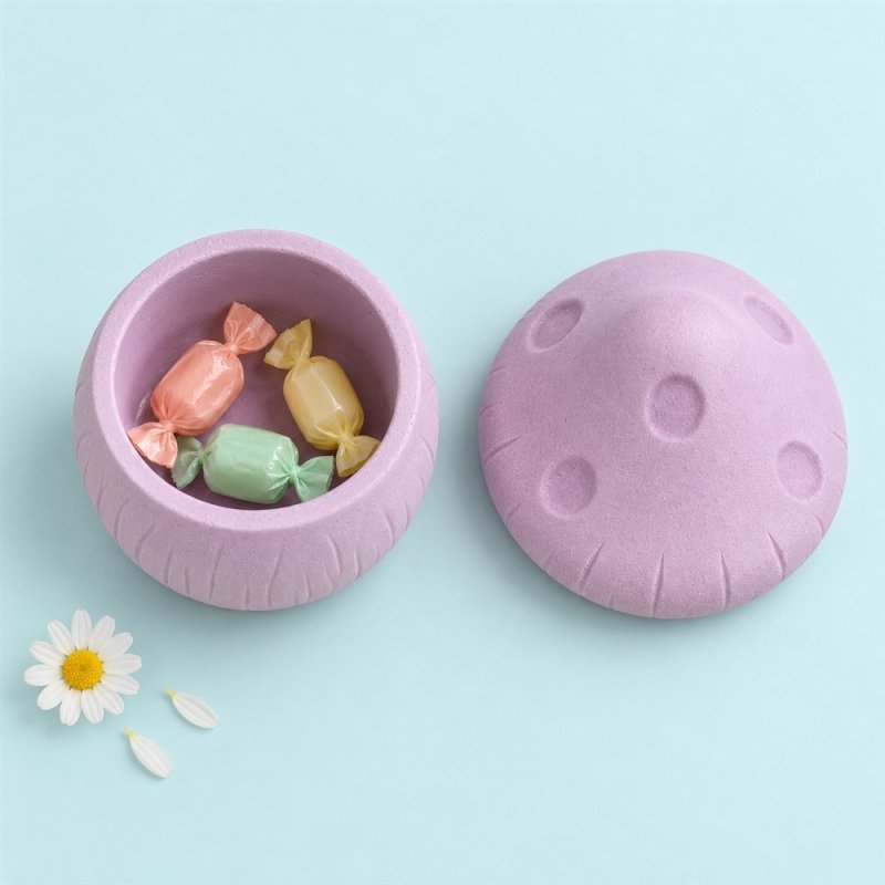 Récipient lilas en forme de champignon avec des bonbons et son couvercle à côté, vu du dessus