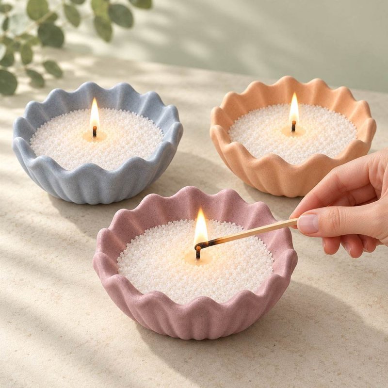 Trois récipients en forme de coquillage cannelé bleus, orange et lilas avec des bougies allumées