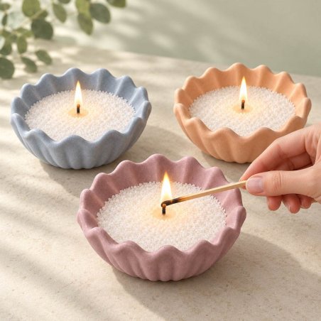 Três recipientes em forma de concha canelada em azul, laranja e lilás com velas acesas