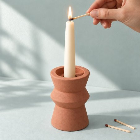 Mano encendiendo una vela alargada en un portavelas terracota de un anillo