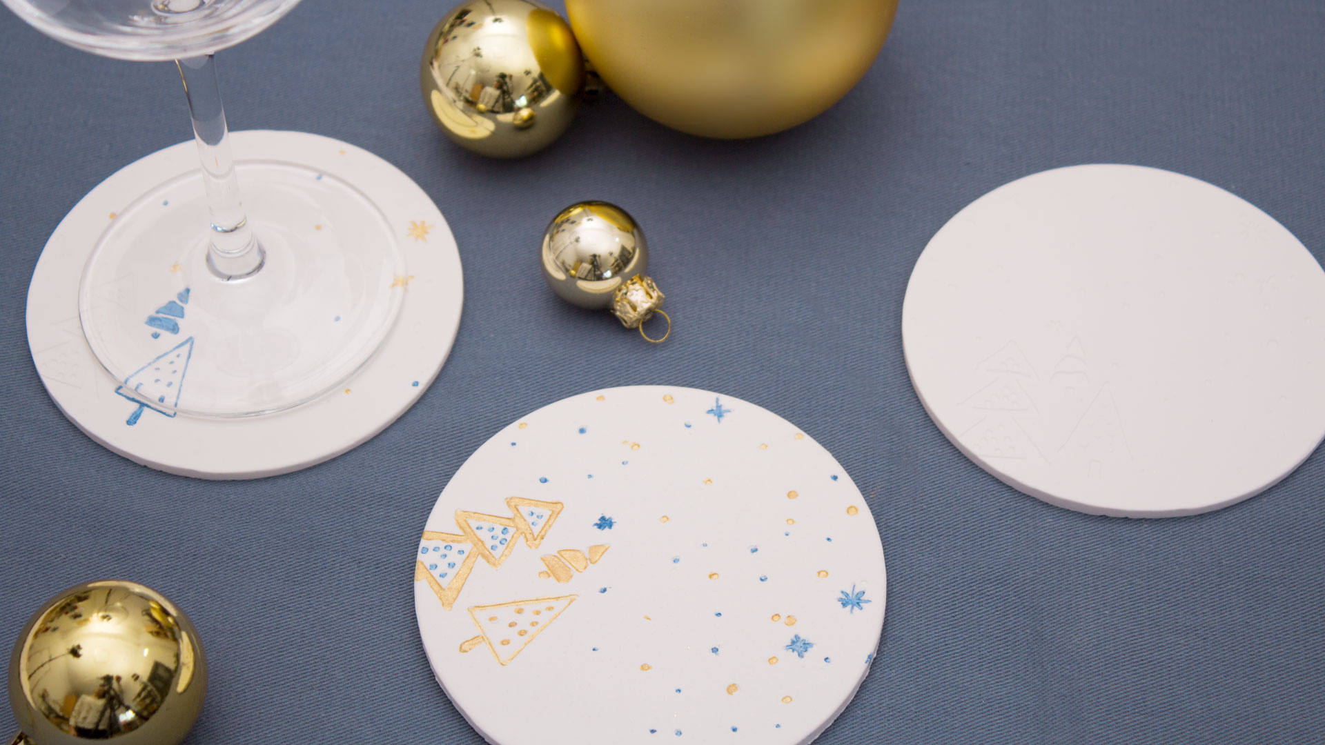 Posavasos navideños terminados con árboles dorados y azules, una copa y bolas de Navidad