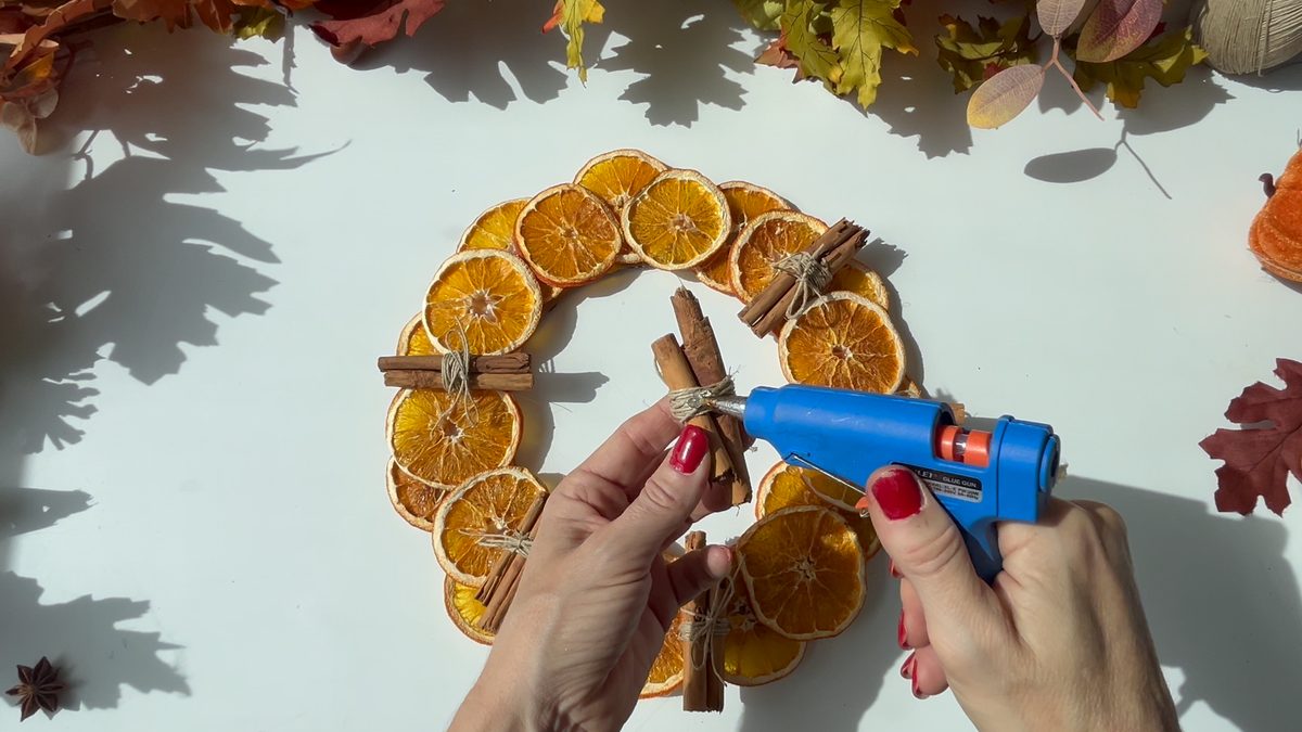 Pegando con silicona caliente los atadillos de canela sobre la corona de naranjas
