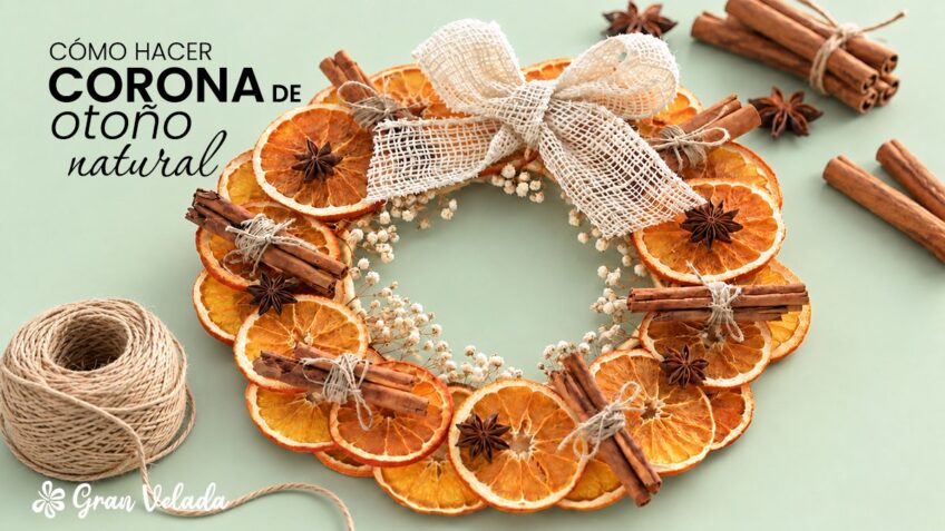 Corona de otoño natural con rodajas de naranja deshidratada, canela, anís estrellado y lazo de yute sobre fondo verde menta