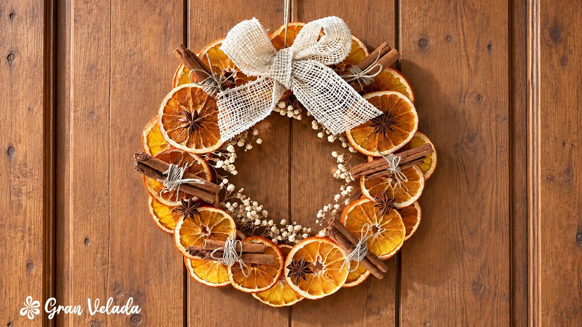 Corona de otoño natural colgada en una puerta de madera con naranja deshidratada, canela y lazo de yute