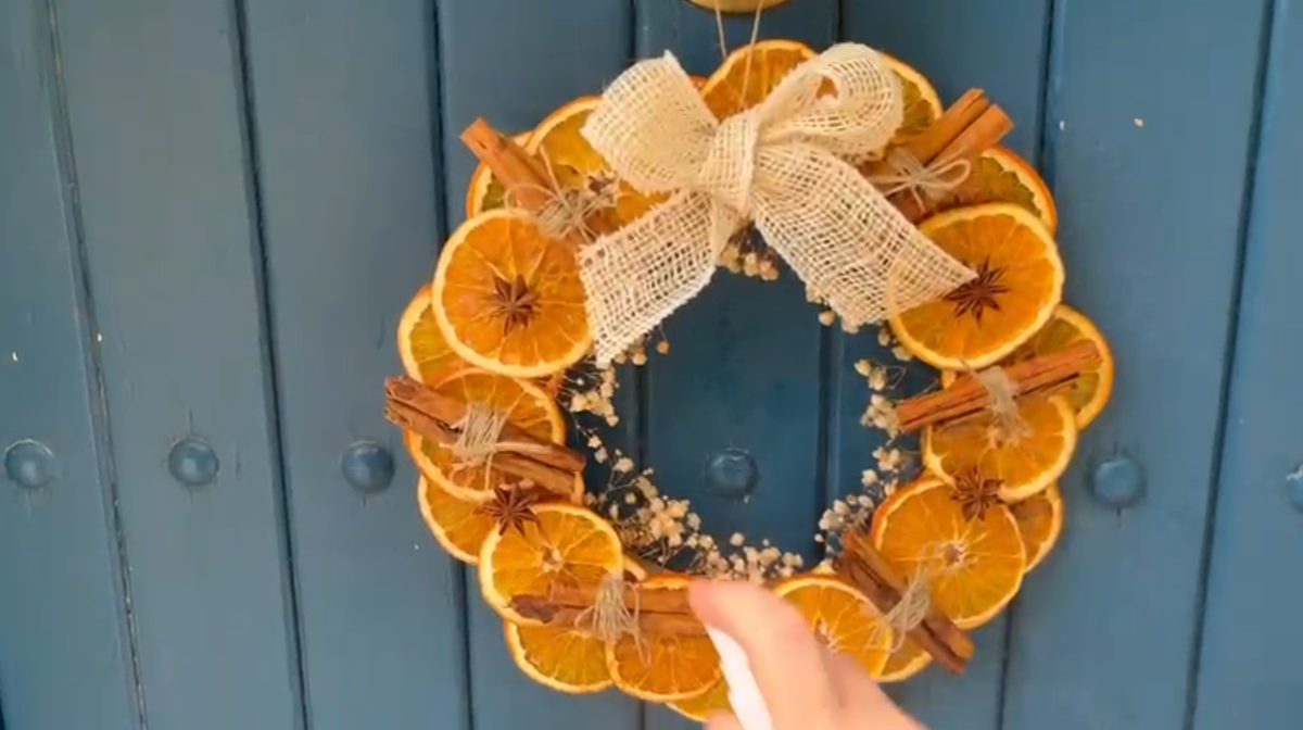 Pulverizando el spray aromático sobre la corona de otoño colgada en la puerta
